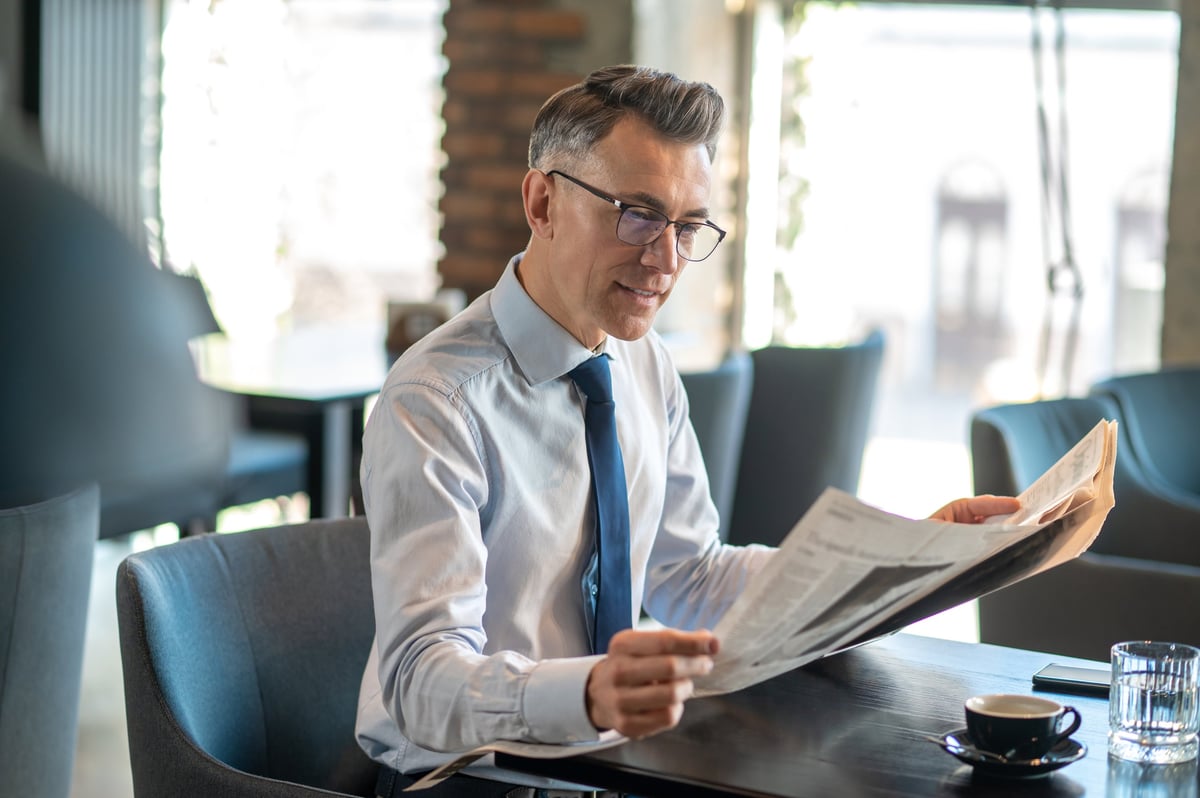 Directivo leyendo un periódico en una cafetería, monitoreando la conversación mediática